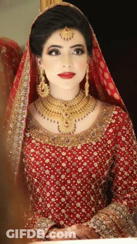 A Woman In A Red Dress And Gold Jewelry Is Looking At Herself In The Mirror GIF