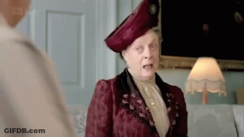 A Woman In A Red Dress And Hat Is Standing Next To A Lamp And Talking To Another Woman . GIF