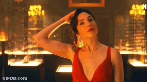 A Woman In A Red Dress And Necklace Is Standing In A Room With Her Hand On Her Head . GIF