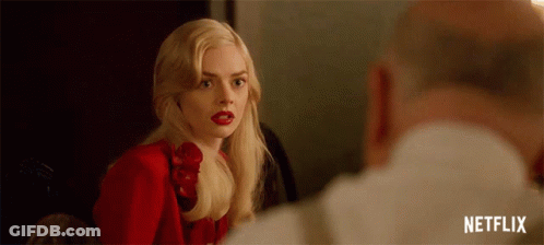 A Woman In A Red Dress And Red Lipstick Is Looking At A Man In A White Shirt . GIF