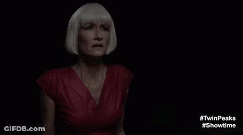 A Woman In A Red Dress And White Hair Is Standing In The Dark . GIF
