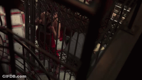 A Woman In A Red Dress Is Behind Bars In A Dark Room GIF