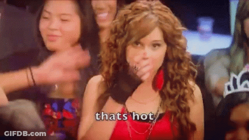 A Woman In A Red Dress Is Covering Her Mouth With Her Hand While A Crowd Of People Applaud . GIF