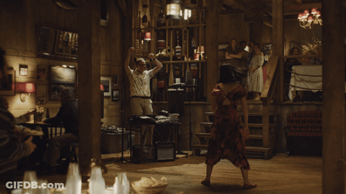 A Woman In A Red Dress Is Dancing In A Room With People GIF