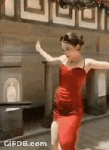 A Woman In A Red Dress Is Dancing On A Sidewalk . GIF