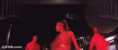 A Woman In A Red Dress Is Dancing On A Stage With A Man In A Red Shirt Behind Her GIF
