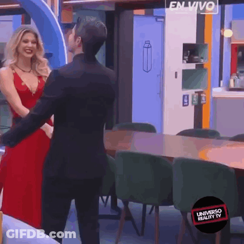 A Woman In A Red Dress Is Dancing With A Man In A Black Suit In A Room That Says Universo Reality TV GIF