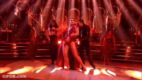 A Woman In A Red Dress Is Dancing With A Man On A Stage GIF