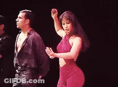 A Woman In A Red Dress Is Dancing With A Man On A Stage . GIF
