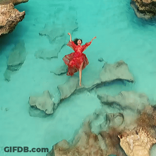A Woman In A Red Dress Is Floating In A Body Of Water GIF