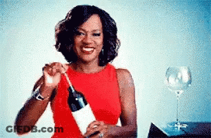 A Woman In A Red Dress Is Holding A Bottle Of Wine . GIF