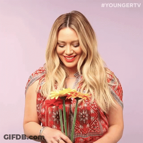 A Woman In A Red Dress Is Holding A Bouquet Of Flowers With The Hashtag #Youngertv GIF