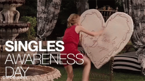 A Woman In A Red Dress Is Holding A Large Heart Shaped Pillow GIF