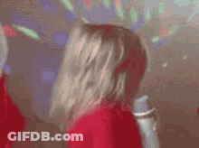 A Woman In A Red Dress Is Holding A Microphone And Dancing In A Disco Room . GIF