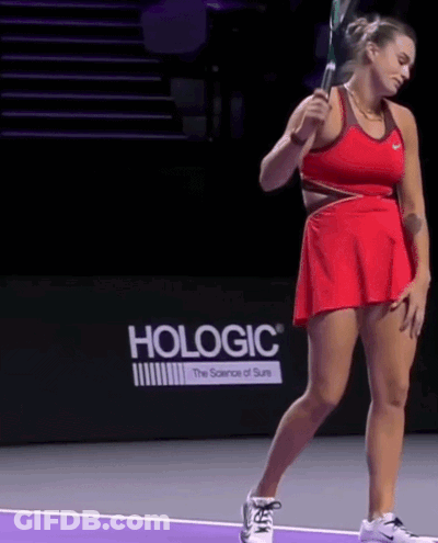 A Woman In A Red Dress Is Holding A Tennis Racquet In Front Of A Hologic Sign GIF