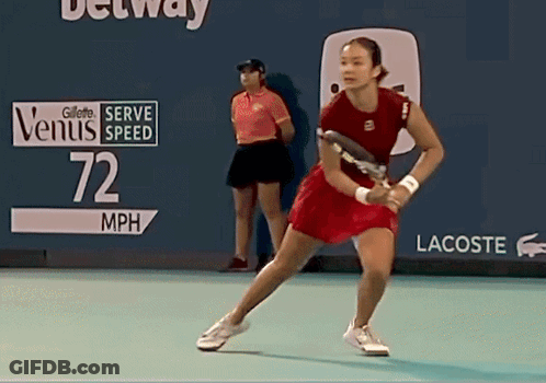 A Woman In A Red Dress Is Holding A Tennis Racquet In Front Of A Sign That Reads 72 Mph GIF
