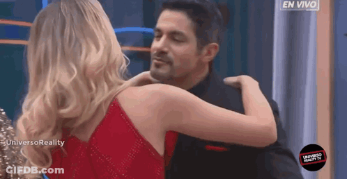 A Woman In A Red Dress Is Hugging A Man In A Black Shirt GIF