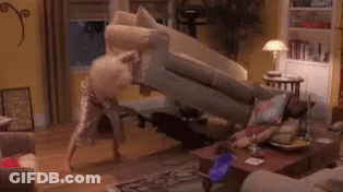 A Woman In A Red Dress Is Kneeling On A Couch In A Living Room With A Vacuum Cleaner . GIF