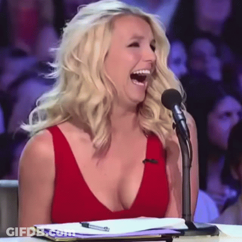 A Woman In A Red Dress Is Laughing While Sitting At A Microphone GIF