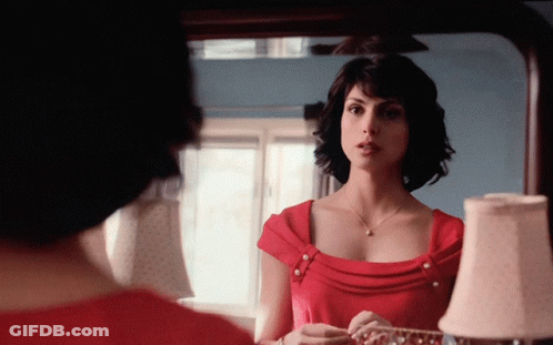 A Woman In A Red Dress Is Looking At Her Reflection In A Mirror GIF