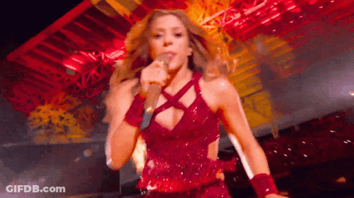 A Woman In A Red Dress Is Singing Into A Microphone . GIF