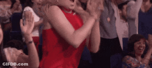 A Woman In A Red Dress Is Sitting In A Crowd Of People Clapping Their Hands . GIF