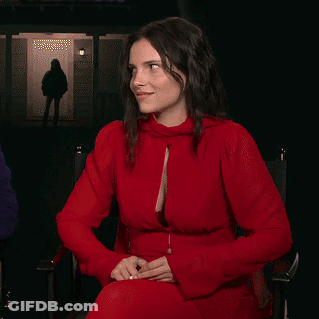 A Woman In A Red Dress Is Sitting In Front Of A Door GIF