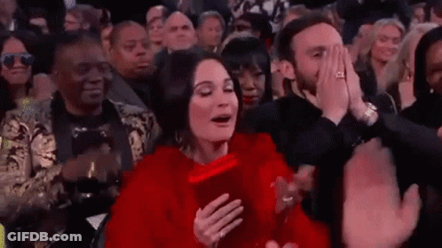 A Woman In A Red Dress Is Sitting In The Audience At A Concert . GIF