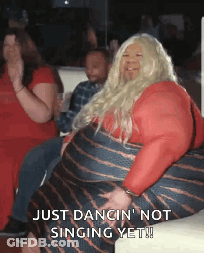 A Woman In A Red Dress Is Sitting On A Couch And Says Just Dancin ' Not Singing Yet ! GIF