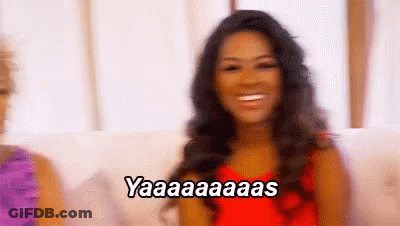 A Woman In A Red Dress Is Sitting On A Couch And Smiling While Saying Yaaa . GIF