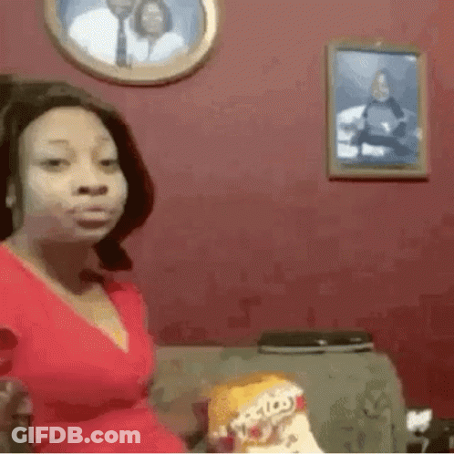 A Woman In A Red Dress Is Sitting On A Couch Holding A Bag Of Doritos Chips . GIF