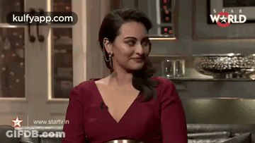 A Woman In A Red Dress Is Sitting On A Couch In A Living Room . GIF
