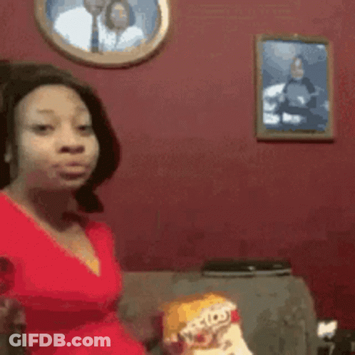 A Woman In A Red Dress Is Sitting On A Couch In Front Of A Picture Of A Man And Woman . GIF