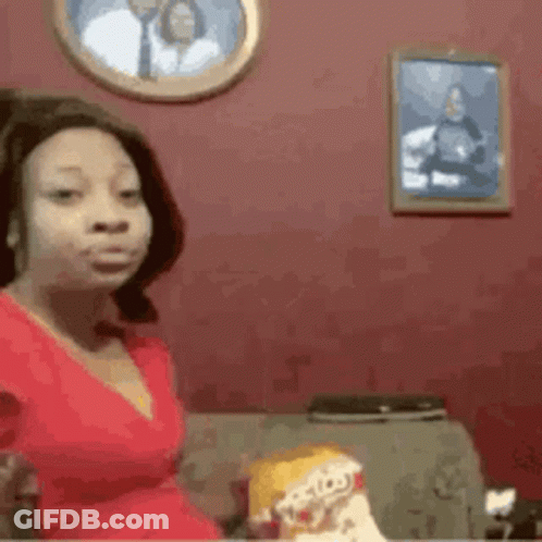 A Woman In A Red Dress Is Sitting On A Couch With A Picture Of A Man On The Wall Behind Her . GIF