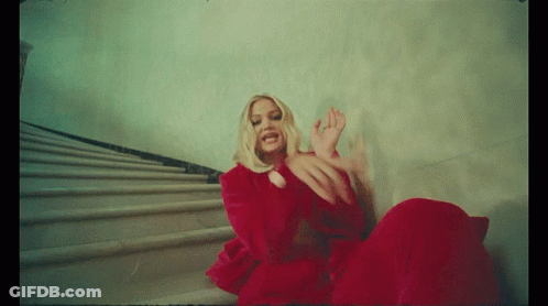 A Woman In A Red Dress Is Sitting On Some Stairs GIF