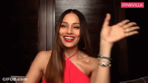 A Woman In A Red Dress Is Smiling And Waving Her Hand . GIF