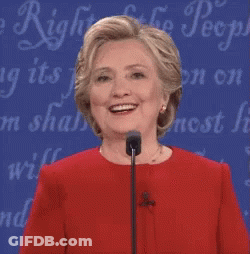 A Woman In A Red Dress Is Smiling In Front Of A Sign That Says ' Freedom Of The People ' GIF