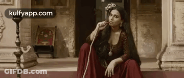 A Woman In A Red Dress Is Smoking A Hookah While Sitting On The Steps Of A Building . GIF