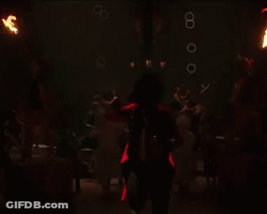 A Woman In A Red Dress Is Spinning A Hula Hoop With Fireworks Behind Her GIF