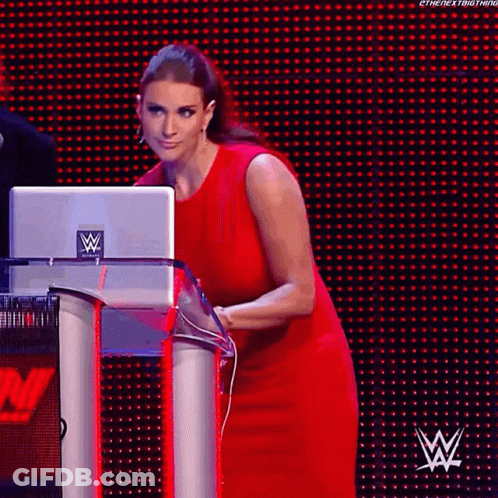 A Woman In A Red Dress Is Standing Behind A Podium With A Laptop On It . GIF