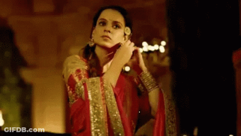 A Woman In A Red Dress Is Standing In A Dark Room Holding A Flower In Her Hand . GIF