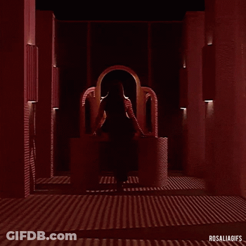 A Woman In A Red Dress Is Standing In A Dark Room With A Red Light Behind Her . GIF