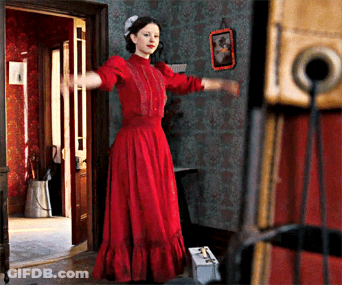 A Woman In A Red Dress Is Standing In A Doorway With Her Arms Outstretched GIF