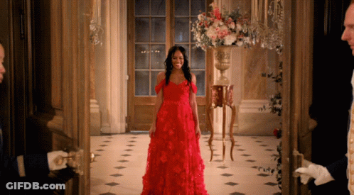 A Woman In A Red Dress Is Standing In A Doorway GIF