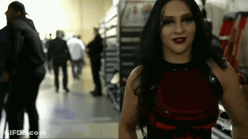 A Woman In A Red Dress Is Standing In A Hallway With People Walking Behind Her . GIF