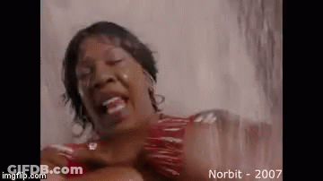 A Woman In A Red Dress Is Standing In A Shower And Laughing . GIF