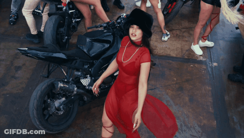 A Woman In A Red Dress Is Standing In Front Of A Black Motorcycle GIF