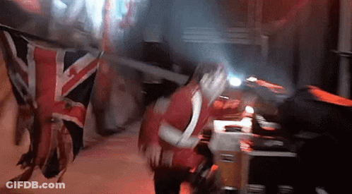 A Woman In A Red Dress Is Standing In Front Of A British Flag . GIF