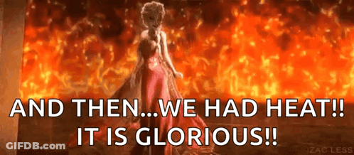 A Woman In A Red Dress Is Standing In Front Of A Fire With The Words And Then We Had Heat ! It Is Glorious ! GIF