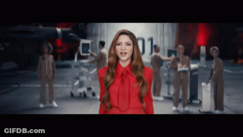 A Woman In A Red Dress Is Standing In Front Of A Group Of People With The Number 01 Behind Her GIF